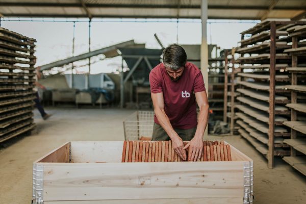 Un trabajador colocando baldosas artesanales de barro en un palet con cercos de madera retornable.